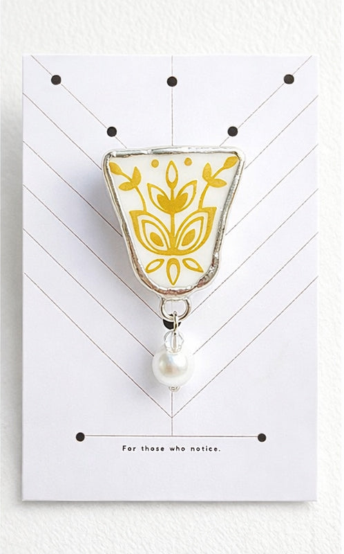 Decorative brooch with floral design and pearl on a white card